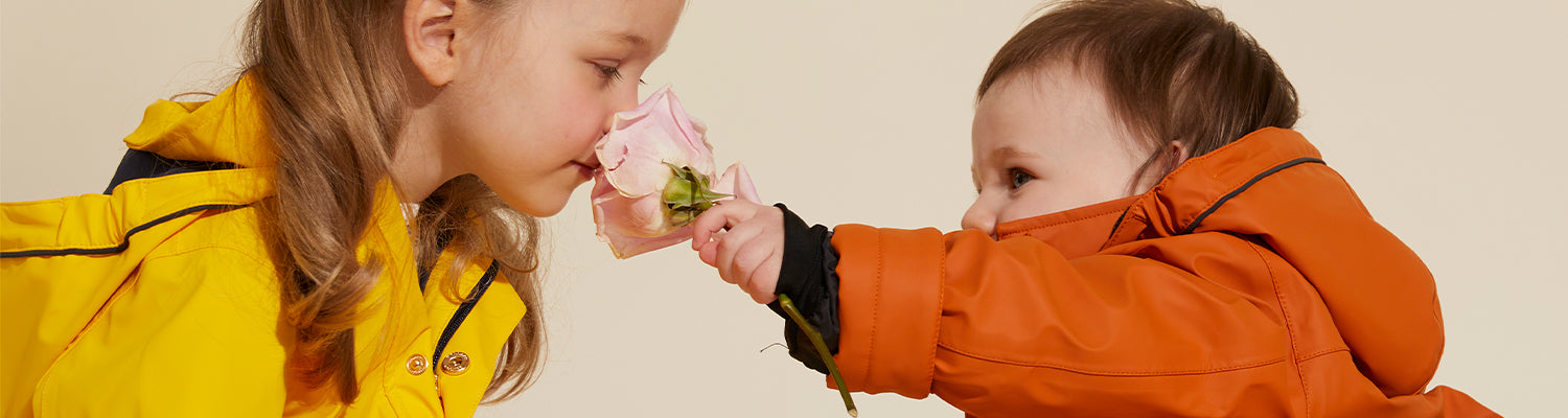 Little girl smells pink rose in childrens yellow rain jacket little girl holding rose in childrens orange rain jacket